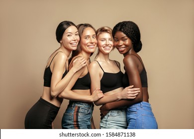 Multi Ethnic Group Of Womans With Diffrent Types Of Skin Standing Together And Looking On Camera. Diverse Ethnicity Women - Caucasian, African And Asian Against Beige Background