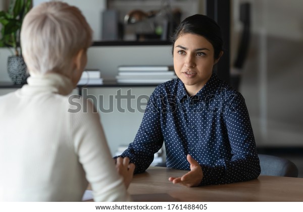 Multi ethnic indian and caucasian diverse young\
businesswomen sitting in front of each other in office during\
business meeting. HR manager and vacancy candidate talk, job\
interview and hiring\
concept