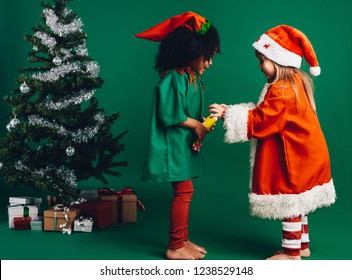 Multi ethnic kids playing with a toy standing beside a decorated christmas tree. Little girls looking at their christmas gift.