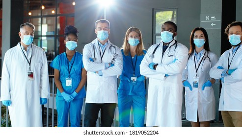 Multi ethnic male and female doctors. International medics in medical masks. Protected workers. Mixed-races physicians and nurses looking at camera. Clinic team. Docs at work in hospital.
