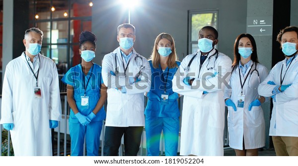 Multi\
ethnic male and female doctors. International medics in medical\
masks. Protected workers. Mixed-races physicians and nurses looking\
at camera. Clinic team. Docs at work in\
hospital.