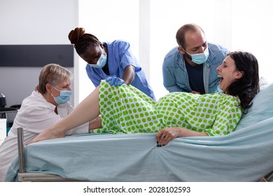 Multi ethnic medical team delivering child and woman pushing in hospital ward bed. Adult with painful contractions giving birth to baby while doctor, nurse and husband assisting - Powered by Shutterstock