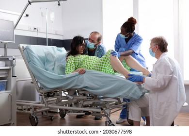 Multi ethnic medical team helping with child delivery in hospital ward. Woman giving birth to baby while laying in bed with labor contractions. Doctor and black nurse assisting birth - Powered by Shutterstock