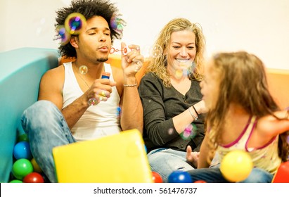 Multi Ethnic Parents Playing With Daughter Inside Ball Pit Swimming Pool - Happy People Having Fun In Children Playground Indoor - Family And Love Concept - Focus On Woman Face - Warm Filter