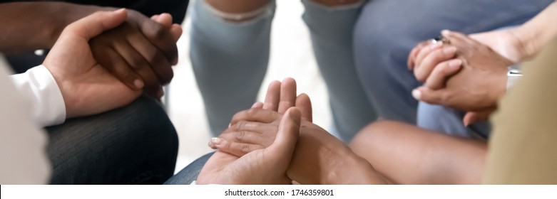Multi ethnic people sit in circle hold hands during group therapy session close up horizontal photo banner for website header design. Psychological support, people overcome addiction together concept