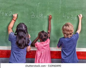 Multi ethnic primary school classroom writing with chalk at blackboard.