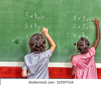 Multi ethnic primary school classroom writing with chalk at blackboard.