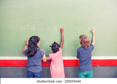 Multi Ethnic Schoolmates Writing Math At Chalkboard.