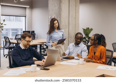 Multi ethnic team collaborating, sharing insights while using digital devices in modern, open concept office environment