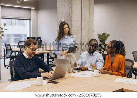 Multi ethnic team collaborating, sharing insights while using digital devices in modern, open concept office environment