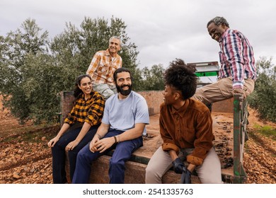 Multi ethnic team of farmers taking a break, sitting and talking on a truck during the olive harvest in a sunny orchard, enjoying the moment of rest and sharing their work experience - Powered by Shutterstock