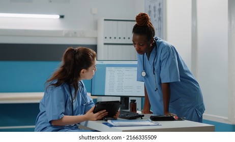 Multi Ethnic Team Of Nurses Looking At Digital Tablet For Consultation And Treatment. Diverse Group Of Medical Assistants Working With Technology For Healthcare System And Checkup.