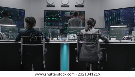 Multi ethnic team of traders work on multi-monitor computers with displayed real-time stocks. Colleagues analyze exchange market charts on big screens. Cryptocurrency trading and investment. Zoom out.