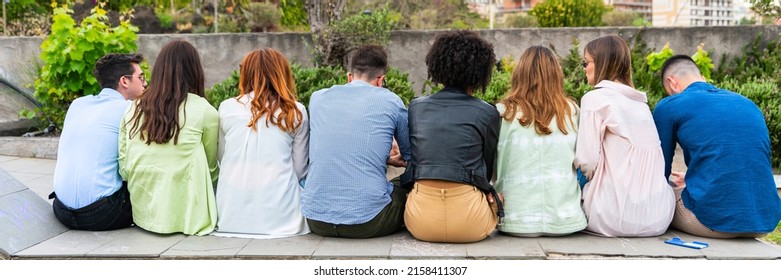Multi ethnic young people sitting on a bench in a park from behind - shot from behind their backs - Wait concept – group person from back side – look from behind – rear view -  view of people behind p