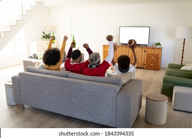 Multi Generation African American Family At Home Sitting On Sofa In Living Room, Watching Sports On TV Cheering With Arms In The Air. Family Spending Quality Time At Home Together In Slow Motion.