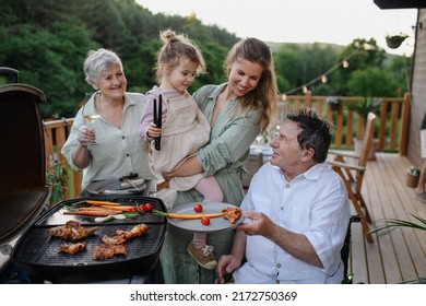 Multi Generation Family Grilling Outside On Patio In Summer During Garden Party