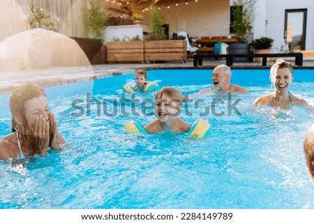 Multi generation family having fun and enjoying swimming in backyard pool during summer holiday.
