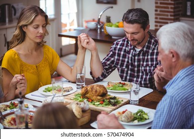 Multi generation family holding hands while praying at dining table in home - Shutterstock ID 570474904