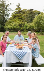 Multi Generation Family At Picnic Table Having Dinner Outside Smiling At Camera