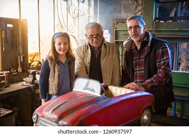 Multi Generation Family Posing For The Photo In The DIY Workshop Of The Grandfather, In Front Of The Old Pedal Car To Repair