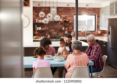 Multi Generation Family Praying Before Meal Around Table At Home