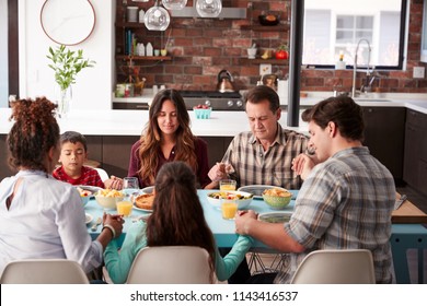 Multi Generation Family Praying Before Meal Around Table At Home