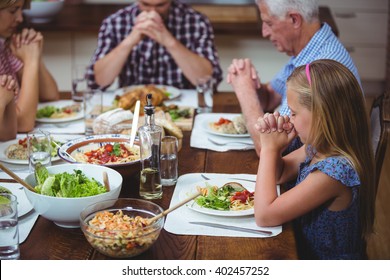 Multi generation family praying with granddad sitting at dining table in home