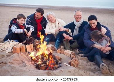 Multi Generation Family Sitting By Fire On Winter Beach