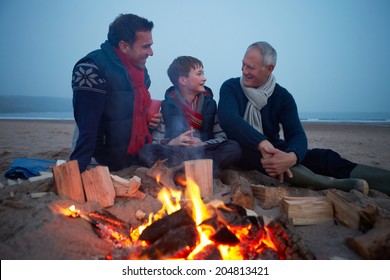 Multi Generation Family Sitting By Fire On Winter Beach