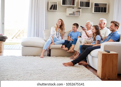 Multi Generation Family Sitting On Sofa At Home Watching TV