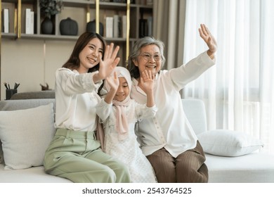 Multi generational asian family bonding at home, grandmother, mother, and daughter waving together, happy family moments, diverse family values, joyful connection, smiling and warmth, candid lifestyle - Powered by Shutterstock