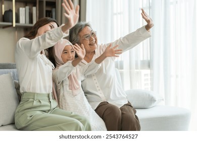 Multi generational asian family bonding at home, grandmother, mother, and daughter waving together, happy family moments, diverse family values, joyful connection, smiling and warmth, candid lifestyle - Powered by Shutterstock