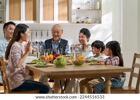 multi generational asian family chatting while having meal together at home