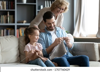 Multi generational family enjoy common hobby, aged woman grandmother looking with love her adult son his little daughter knitting seated on couch in living room, pastime, spend time together concept - Powered by Shutterstock