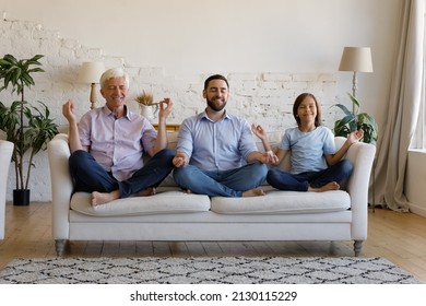 Multi Generational Family, Older 50s Man His Adult Son And Little Grandson Meditating Together Seated Cross-legged On Couch. Healthy Life Habit, Lifestyle, Yoga Training On Quarantine At Home Concept