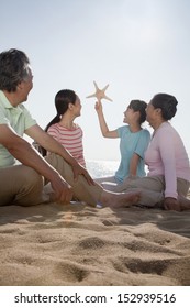 Multi Generational Family Sitting On The Beach Looking At Starfish