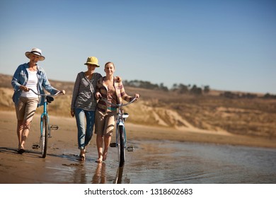 Multi Generational Family Walking Their Bikes On A Beach.