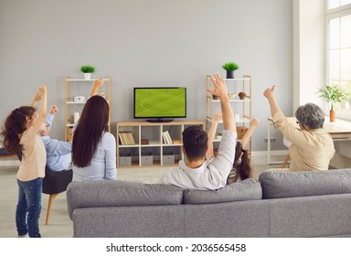 Multi generational family watching football on television. View from behind three generations sitting on sofa enjoying World Cup soccer match on LED LCD plasma TV screen in modern living room interior