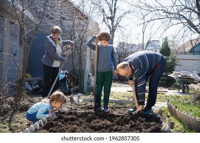 Multi Generational Family Work Together In The Garden And Open The Beds With A Shovel Near The House. Slow Life. Enjoy The Little Things. 