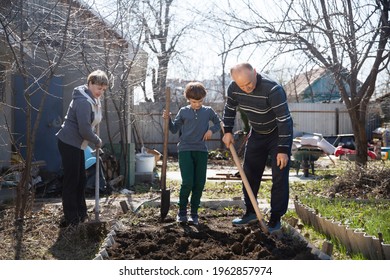 Multi Generational Family Work Together In The Garden And Open The Beds With A Shovel Near The House. Slow Life. Enjoy The Little Things. 