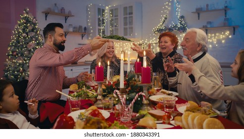 Multi Generational Members Of Happy Family Gathering At Table On Christmas Festive And Sharing Delicious Dishes In Cozy Living Room