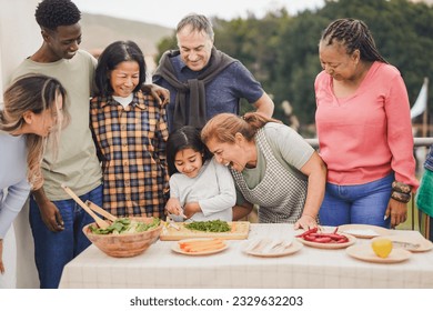 Multi generational people cooking at house rooftop - Multiracial friends preparing food with female child outdoor during weekend day - Grandmother having fun with granddaughter - Powered by Shutterstock