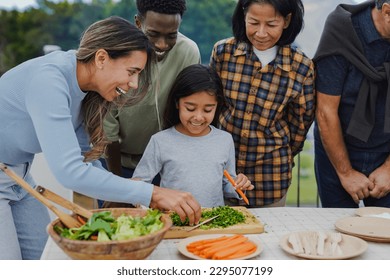 Multi generational people cooking together at home terrace rooftop - Multiracial friends cutting vegetable with  female child outdoor during weekend day - Powered by Shutterstock