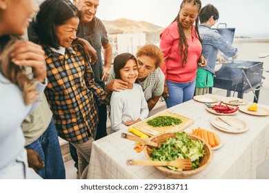 Multi generational people doing barbecue at home's rooftop - Multiracial friends having fun eating and cooking during weekend day - Summer and food concept - Main focus on african woman face - Powered by Shutterstock