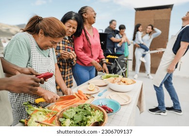 Multi generational people doing barbecue at home's rooftop - Multiracial friends having fun eating and cooking together during weekend day - Summer and food concept - Main focus on latin woman face - Powered by Shutterstock