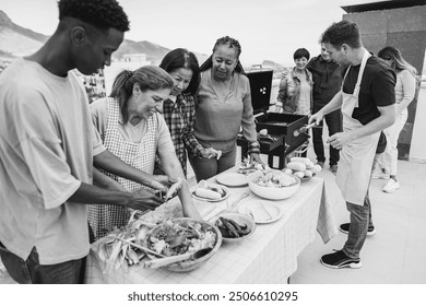 Multi generational people doing barbecue at home's rooftop - Multiracial friends having fun eating and cooking together during weekend day - Black and white editing - Main focus on african woman face - Powered by Shutterstock