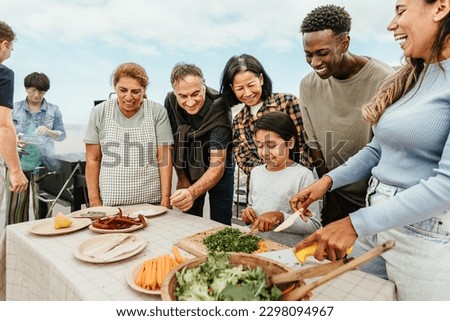 Multi generational people having fun doing barbecue at house rooftop - Happy multiracial friends cooking together - Summer gatherings and food concept