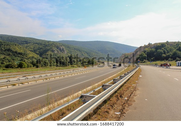 A multi lane road in a\
Sunny color running between mountains covered with green forest\
with single cars