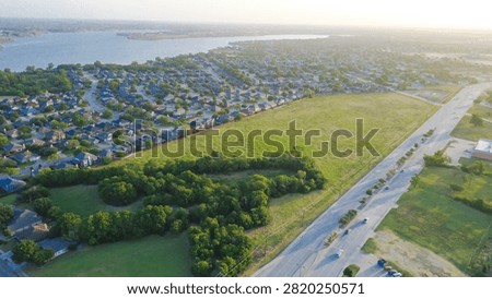 Multi lane thoroughfares buffer lush green fields and dense residential grids adjacent to Lakewood Estates. Vast lake inlets extend across the far horizon past Little Elm, suburbs DFW, Texas. USA