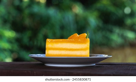 Multi layer orange cake topped with orange marmalade, sliced ​​orange and rosemary leaves. Placed in a plate and with a spoon placed on its side.Coffee time. Eat with hot coffee.